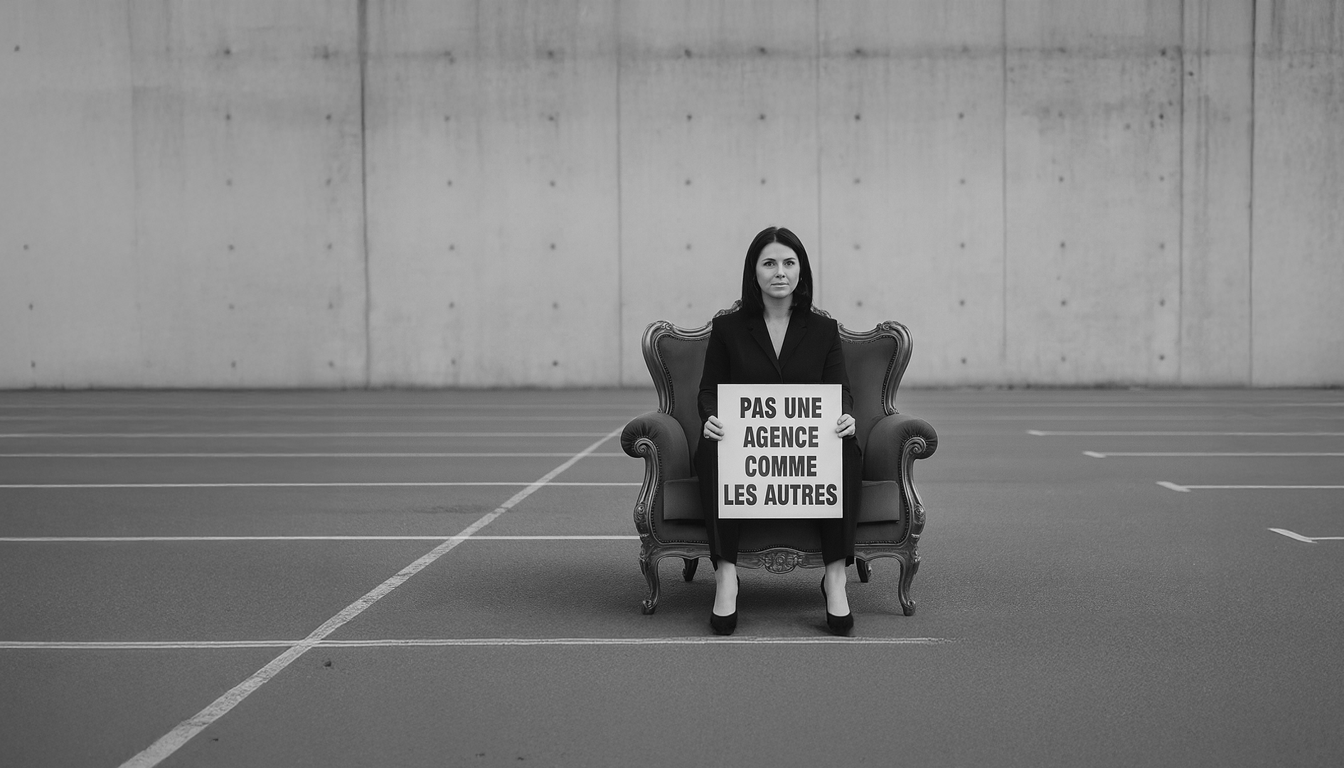Publicité Neufchâtel en Bray Femme en costume assise sur un canapé, tenant une pancarte dans un espace vide.