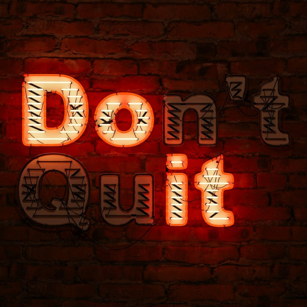 Jeu concours VISUELROUGE community management Texte en néon sur mur en briques : "Don't Quit".